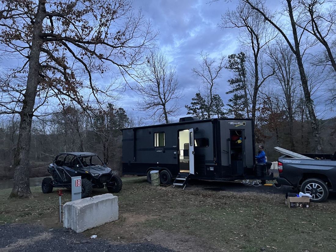 A side-by-side and a camper parked under bare trees