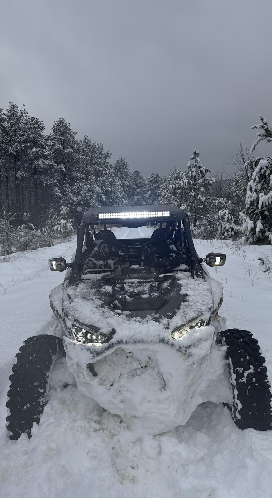 A side-by-side with its light bar on, parked in deep snow on a wooded trail
