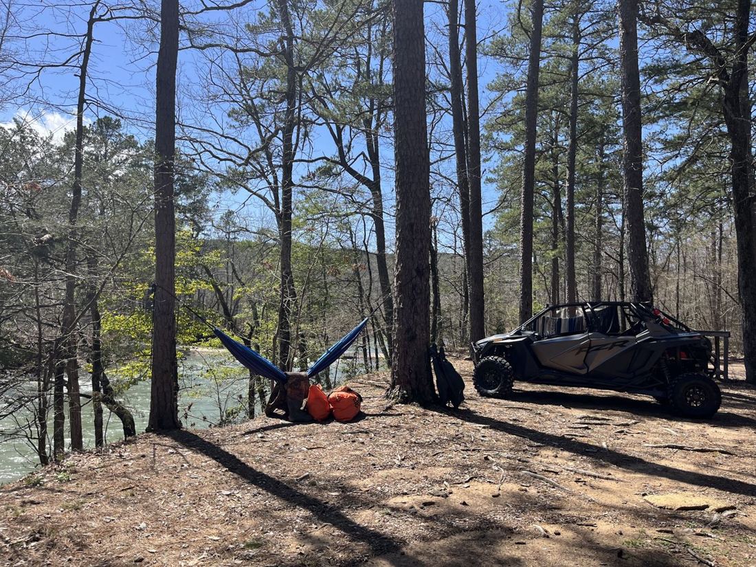 A hammock strung between pines above the river, a side-by-side parked nearby